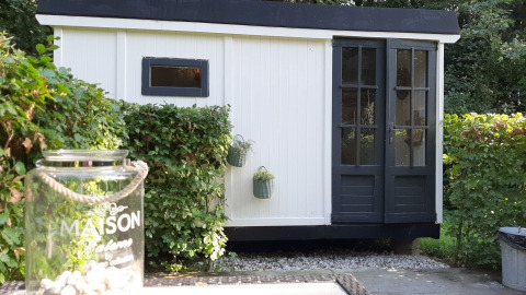 Schwarz-weißes Lodge namens Pipo Maison bei Buytenplaets Suydersee in den Niederlanden, von Büschen umgeben.