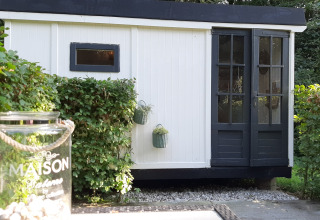 Schwarz-weißes Lodge namens Pipo Maison bei Buytenplaets Suydersee in den Niederlanden, von Büschen umgeben.