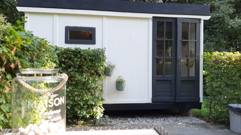 Casa lodge en blanco y negro llamada Pipo Maison en Buytenplaets Suydersee, Países Bajos, rodeada de setos verdes.