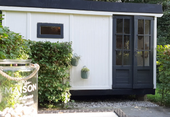 Lodge noir et blanc nommé Pipo Maison à Buytenplaets Suydersee aux Pays-Bas, entouré de haies vertes.