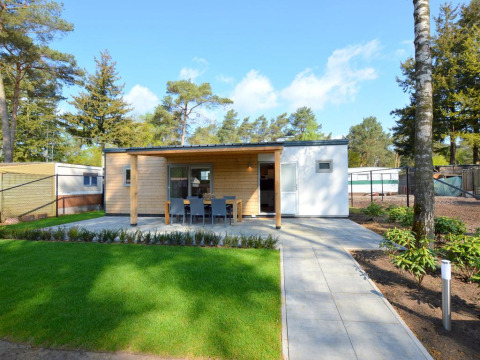 Lodge moderne avec façade bois, terrasse et coin repas extérieur, entouré de pelouse et d’arbres.