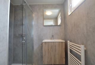 Baño moderno de una cabaña con paredes grises, ducha de cristal, mueble de madera, espejo y ventana.