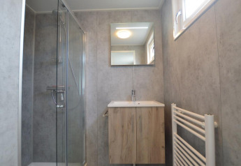 Bagno moderno in un lodge con pareti grigie, box doccia, mobile in legno, specchio e finestra.