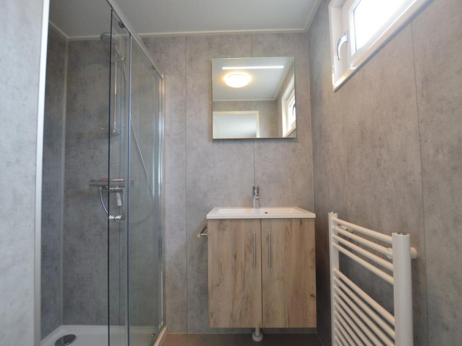 Baño moderno de una cabaña con paredes grises, ducha de cristal, mueble de madera, espejo y ventana.