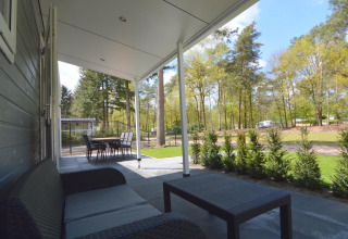 Overdekt terras met lounge en tafel bij Easy chalet, Eurocamping Vessem BV, uitkijkend op het bosrijke groen.