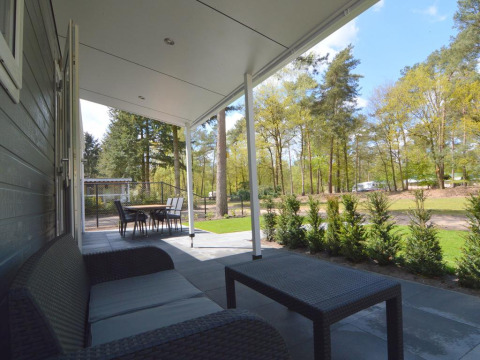 Veranda coperta con divano e tavolo, vista su alberi e siepi presso Easy chalet a Eurocamping Vessem BV.