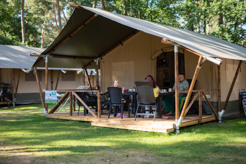 Famiglia rilassata sulla veranda di una tenda safari con servizi igienici a Eurocamping Vessem nei Paesi Bassi.