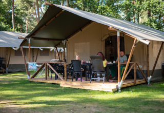Famiglia rilassata sulla veranda di una tenda safari con servizi igienici a Eurocamping Vessem nei Paesi Bassi.