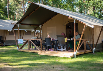 Familie nyder udendørs måltid på terrassen foran en safaritelt med sanitære faciliteter i Eurocamping Vessem.