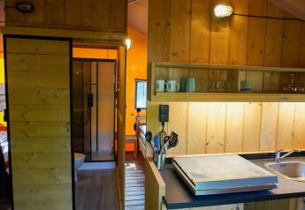 Interieur van een safaritent met houten wanden, kitchenette, gootsteen en een badkamer met douche.