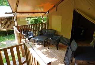Buiten zitruimte met plastic stoelen op houten terras aan een safaritent bij Camping Pittoresque in Frankrijk.