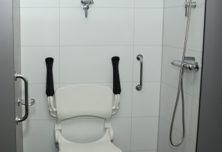Handicapvenlig brusekabine med stol, støttestænger og brusehoved i et feriehus i Costa Kabrita, Nederlandene.