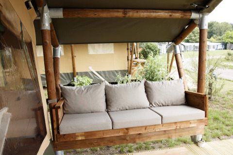 Banc en bois avec coussins beige devant une tente safari au Costa Kabrita, aux Pays-Bas.