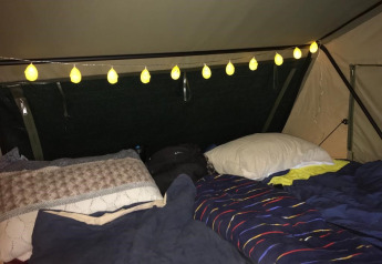 Gemütliches Zeltinterieur mit Kissen, Decken und Lichterkette bei Treelodge im Costa Kabrita, Niederlande.