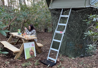 Persoon aan picknicktafel voor Treelodge-boomhut met ladder in bos bij Costa Kabrita, Nederland.