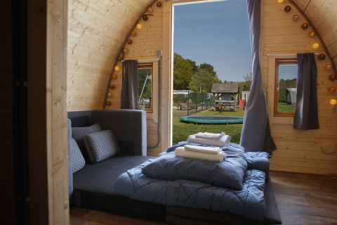 Cozy Glamping Pod at Costa Kabrita in the Netherlands with a double bed, sofa, and playground view outside.
