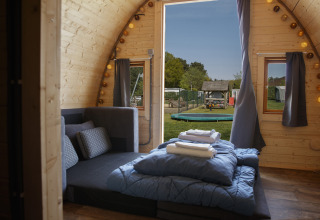 Cozy Glamping Pod at Costa Kabrita in the Netherlands with a double bed, sofa, and playground view outside.