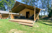 Tienda safari con terraza y baños en Camping de Tolbrug, Países Bajos, rodeada de naturaleza y árboles.