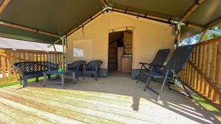 Safari tent with wooden deck, plastic chairs and tables, and private sanitary facilities inside.