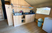 Kleine keuken in een safaritent met houten kasten, gasfornuis, gootsteen, koffiezetapparaat en koelkast.