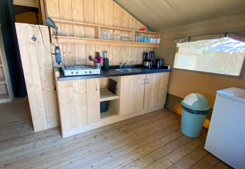 Kleine keuken in een safaritent met houten kasten, gasfornuis, gootsteen, koffiezetapparaat en koelkast.
