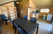 Interieur van een safaritent met eettafel, zes stoelen, kitchenette, open kast en koelkast.