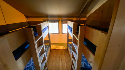 Foto de una habitación de glamping con cuatro literas de madera, ropa de cama azul y suelo de madera.