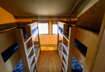 Foto di una stanza glamping con quattro letti a castello in legno, biancheria blu e pavimento in legno.