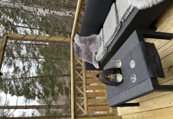 Terraza exterior en Stuga Glamping en Småland Miniglamping, Suecia, con sofá, mesa, copas y vista al bosque.