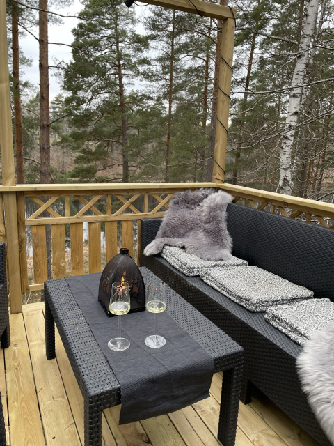 Terrasse von Stuga Glamping bei Småland Miniglamping, Schweden, mit Sofa, Tisch, Gläsern und Waldblick.