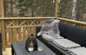 Terraza exterior en Stuga Glamping en Småland Miniglamping, Suecia, con sofá, mesa, copas y vista al bosque.