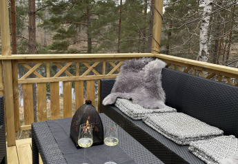 Terrazza esterna presso Stuga Glamping di Småland Miniglamping, Svezia, con divano, tavolo e vista foresta.