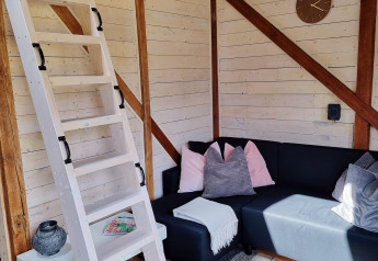 Hyggelig stue i Stuga glamping ved Småland Miniglamping, Sverige, med trætrappe og hjørnesofa.