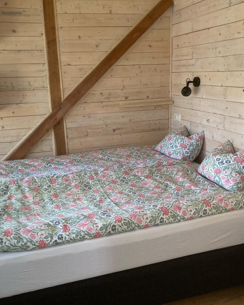 Bed with floral bedding in a wooden cabin room at Stuga glamping at Småland Miniglamping in Sweden.