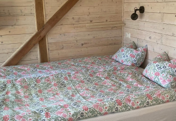 Cama con ropa de cama floral en una cabaña de madera en Stuga glamping de Småland Miniglamping, Suecia.