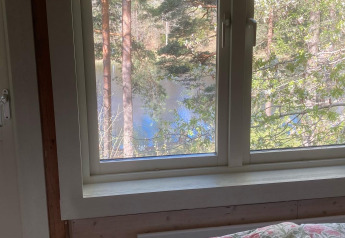 Blick aus einem Stuga-Glamping-Lodge-Fenster bei Småland Miniglamping, Schweden, mit Wald- und Seesicht.