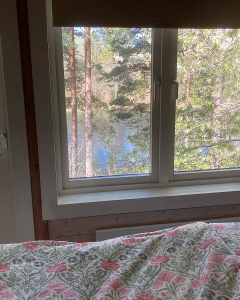 Vista dal letto dello Stuga glamping a Småland Miniglamping, Svezia, verso bosco e lago dalla finestra.