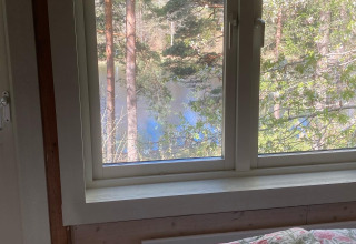 Uitzicht vanuit een bed in Stuga glamping bij Småland Miniglamping, Zweden, raam naar bos en meer.