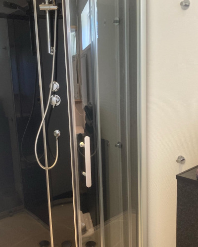 Ducha moderna en cabina de vidrio en Stuga glamping en Småland Miniglamping, Suecia, ambiente limpio y elegante.