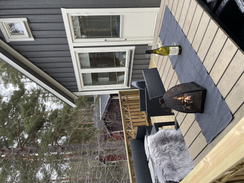 Buitenterras aan Stuga glamping bij Småland Miniglamping, Zweden, met lantaarn en wijnfles op tafel.