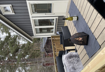 Terraza exterior en Stuga glamping de Småland Miniglamping, Suecia, con linterna y botella de vino en mesa.