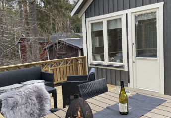 Buitenterras aan Stuga glamping bij Småland Miniglamping, Zweden, met lantaarn en wijnfles op tafel.