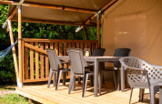 Houten veranda bij een safaritent met kunststof stoelen, tafel en lantaarn onder een canvas dak.