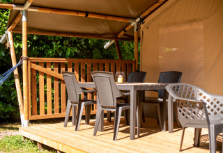 Terrasse en bois devant une tente safari avec chaises en plastique, table et lanterne sous auvent.