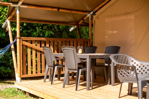 Terrasse en bois devant une tente safari avec chaises en plastique, table et lanterne sous auvent.
