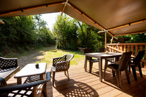 Overdekt houten terras met stoelen aan een safaritent met sanitair op Camping Fargogne, Frankrijk.