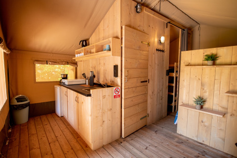 Interieur van een safaritent met houten inrichting en kitchenette bij Camping Fargogne in Frankrijk.