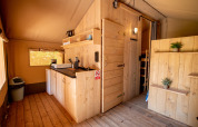 Interieur van een safaritent met houten meubels en kitchenette bij Camping Fargogne in Frankrijk.