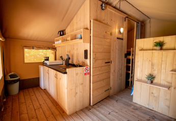 Innenansicht eines Safarizelts mit Holzmöbeln und Küchenbereich auf dem Camping Fargogne in Frankreich.