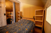 Chambre de tente safari avec lit double, lits superposés, étagères en bois et murs en toile jaune.